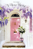 A beautifully composed Brockley doorway scene shows a pale pink front door nestled beneath a trailing canopy of lavender wisteria, creating an intimate feeling of calm and optimism. The door, painted in a light, powdery blush, stands out against softly textured white walls, evoking the characterful facades you might find along the quieter stretches of Brockley Road or near Telegraph Hill. The wisteria above pours down in loose, cascading strands, each one adorned with tiny purple blooms that suggest a gentle, sweet scent lingering in the mild air. On the doorstep sits a modest grey metal bucket, transformed by the florist's touch into a vessel of celebration, filled with lush white and cream roses. The roses are fully open, with plush, layered petals that feel almost touchable, cradled by sprigs of fresh green foliage that soften the arrangement and add a natural, garden-fresh look. Wrapped around the base of the bucket is a soft pink ribbon, tied in a tasteful bow that catches the light and echoes the gentle colours of the door and the blossoms overhead. Sunlight slips through the curtain of wisteria, casting dappled shadows across the stone and giving the whole entrance a warm, late-afternoon glow. The mood is quiet yet full of promise, like the first evening in a new flat when boxes are stacked just inside and everything feels possible. This floral vignette feels perfectly suited to a housewarming or new home gift in Brockley, a tender way to say, may your door always open to love, warmth, and happy memories.