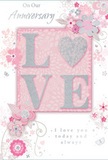 Spread out as if just paired with a fresh anniversary bouquet in Brockley, this card offers a delicate celebration of lasting romance. Its central motif is the word LOVE, crafted in soft, raised letters coated with fine, shimmering glitter, giving the blush-pink characters a subtle sparkle that feels both modern and tender. Each letter is edged with a wash of pearlescent white and touched with silver, so they appear to catch the light much like rose petals in a south London florist's window. The background is a smooth, powdery pink, calm and inviting, allowing the main word and surrounding decoration to stand out without harsh contrast. Flowing from the top and sides, clusters of stylized blossoms and light, curling vines drift across the surface, illustrated in slender lines of blush, mauve, pale grey, and ivory, with small pops of silver foil that twinkle like tiny raindrops on garden leaves near Hilly Fields. These floral details echo the graceful movement of real stems as they arc within a vase, much as we see daily at Brockley Flowers when arranging anniversary stems for homes off Upper Brockley Road or down leafy side streets. Petite petals, swirling embellishments, and nearly hidden butterflies add an air of whimsy, as if a gentle spring breeze were captured on paper. Elegant, understated script conveys messages like On Our Anniversary and I love you today and always, the lettering flowing across the design with the same ease as trailing greenery. The overall mood is one of intimate celebration and heartfelt warmth, making the card feel like a beautifully choreographed companion to a romantic bouquet, perfectly suited to mark another cherished year together in Brockley.